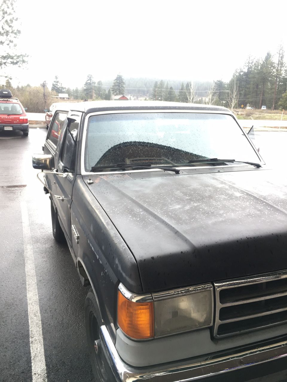 Front passenger side of a dark pickup truck with a chrome bumper and grille, parked on a wet surface.
