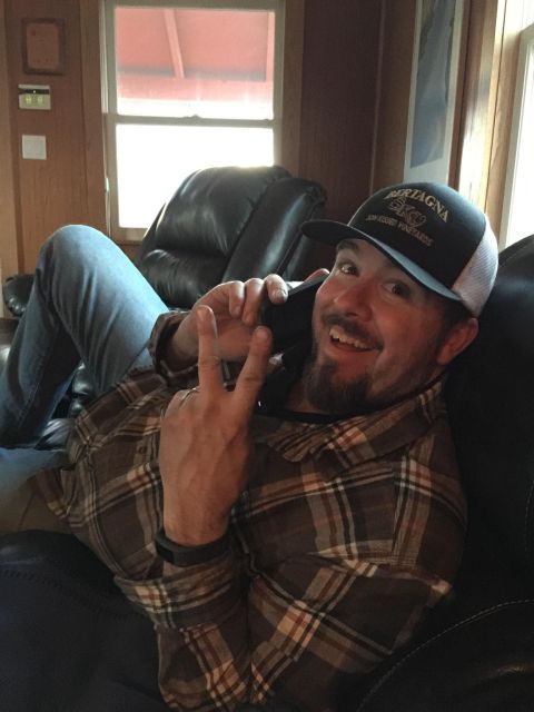 1985 Jeep CJ7 - A man wearing a baseball cap and plaid shirt is lying on a couch and talking on a cell phone while holding up two fingers in a peace sign.