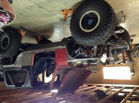 1985 Jeep CJ7 - A red and silver Jeep CJ7 body is upside down and supported by jack stands in a garage. The vehicle has large off-road tires and exposed su…