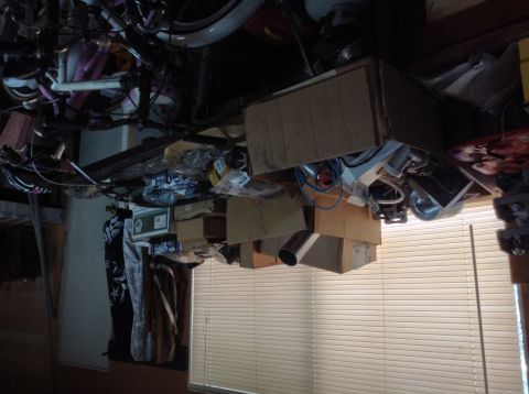 1985 Jeep CJ7 - This image shows a cluttered garage or storage area with bicycles, boxes, and other items stacked high. A window with blinds is visible in…