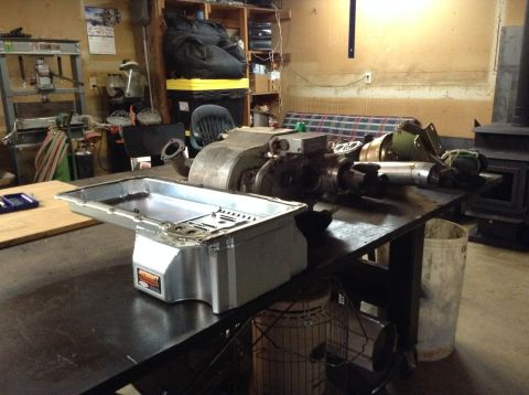 1985 Jeep CJ7 - A metal oil pan with an "AUTOCRAFT" label sits on a workbench in front of a disassembled engine or transmission assembly. Various tools and…