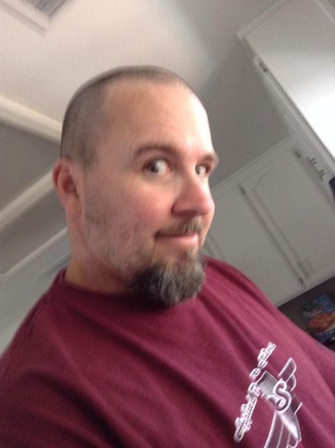 1985 Jeep CJ7 - A man with a shaved head and a goatee is looking over his shoulder at the camera. He is wearing a maroon t-shirt with a graphic design on i…