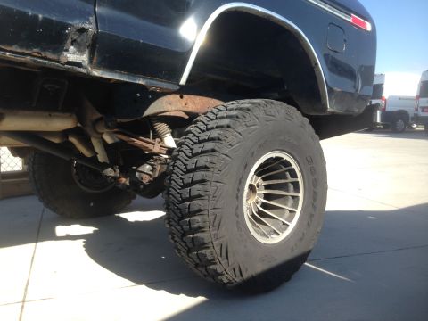 1979 Ford Bronco - A low-angle, close-up shot of the rear passenger side of a black 1979 Ford Bronco, focusing on the large off-road tire and suspension compo…