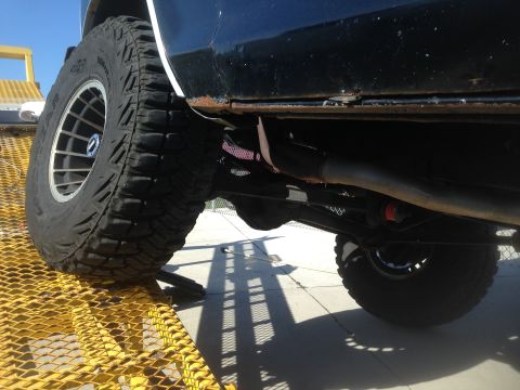 1979 Ford Bronco - Low angle shot of the undercarriage and rear tire of a black Ford Bronco, which is partially on a yellow metal ramp. The vehicle's exhaust…
