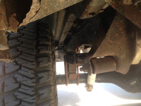 1979 Ford Bronco - The underside of a vehicle shows significant rust on the frame and body panels, with a tire and suspension components visible. A leaf sprin…