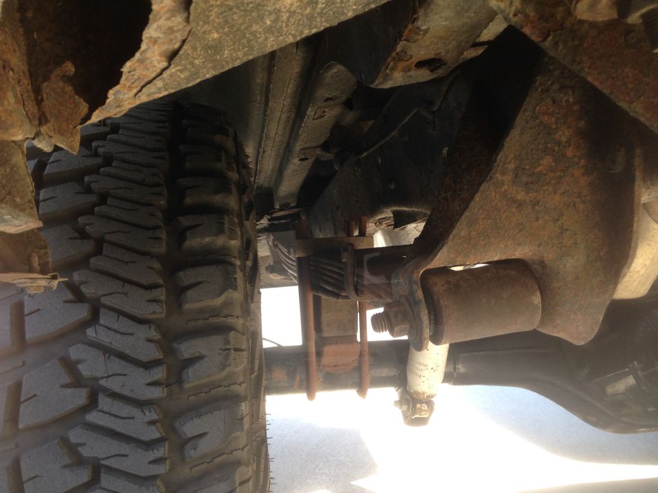Underside of a rusty 1979 Ford Bronco showing tire, leaf spring, and shock absorber.