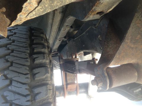 1979 Ford Bronco - Underside view of a vehicle's rear suspension, showing a tire, leaf springs, and heavily rusted frame components.