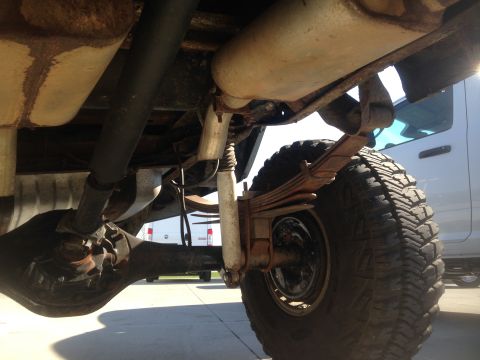 1979 Ford Bronco - The underside of a vehicle shows a leaf spring suspension system, a rear differential, and a driveshaft. A large tire with an aggressive tr…