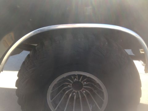 1979 Ford Bronco - A close-up view of the rear wheel well of a dark-colored vehicle, featuring a large off-road tire and a chrome fender flare. The sun is gli…