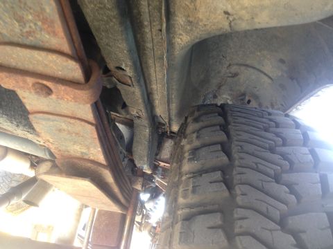 1979 Ford Bronco - Underside view of a vehicle's rear suspension featuring rusty leaf springs and a large tire. The frame and wheel well are visible above the…