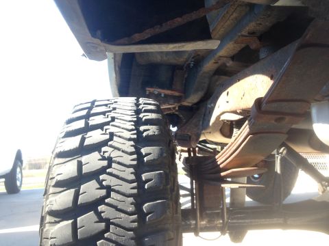 1979 Ford Bronco - A low-angle, close-up view of the undercarriage of a vehicle, focusing on the rear tire and suspension system. The leaf springs and frame c…