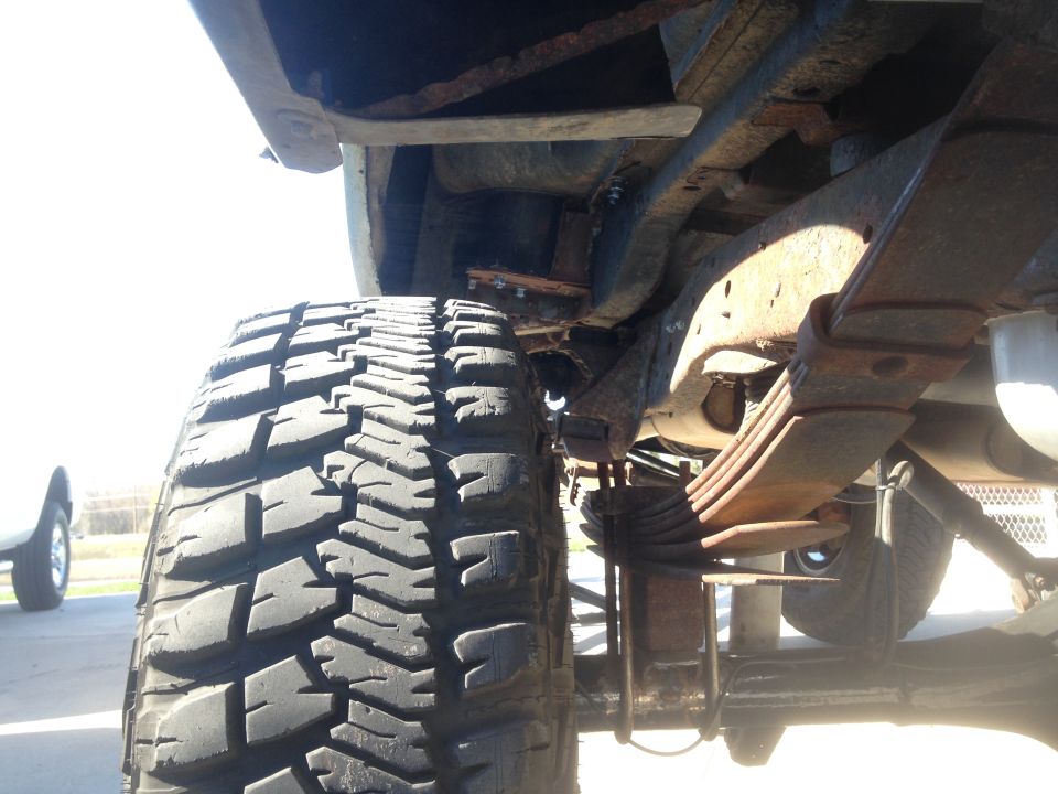 Close-up of a large off-road tire and rusty leaf spring suspension on a vehicle.