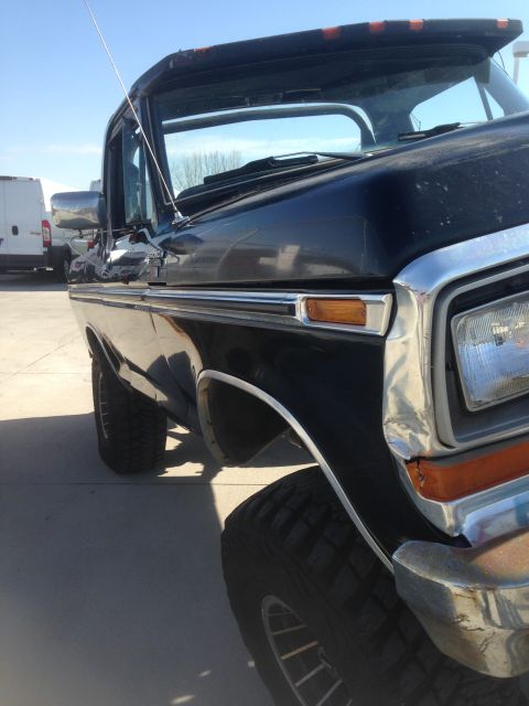 1979 Ford Bronco - The front passenger side of a black 1979 Ford Bronco is shown at a low angle, parked on a concrete surface under a clear blue sky. The vehi…