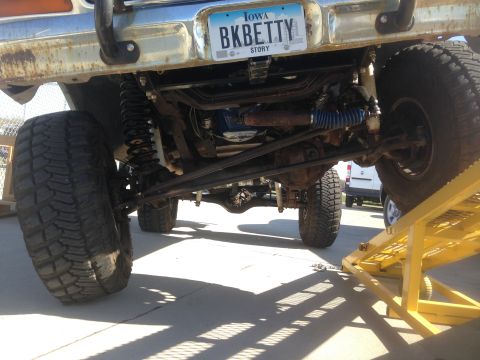 1979 Ford Bronco - The undercarriage of a lifted off-road vehicle, likely a Ford Bronco, is shown with large tires, heavy-duty suspension components, and a cu…
