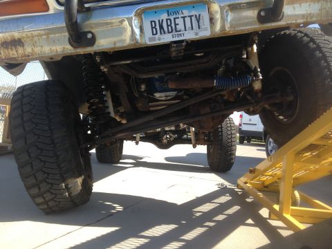 1979 Ford Bronco - The underside of a lifted Ford Bronco is shown, featuring large off-road tires, suspension components, and a custom license plate reading "…