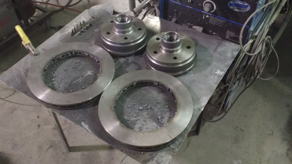 Two brake rotors and two wheel hubs on a metal workbench.