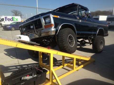 1979 Ford Bronco - A lifted, dark blue 1979 Ford Bronco is parked on a yellow ramp with its front tires elevated. A black toolbox sits on the ground below the…