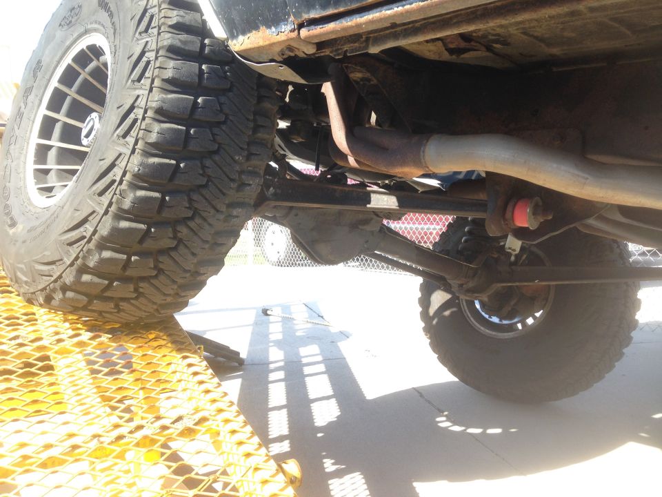 Underside of a lifted vehicle with large off-road tire on a yellow ramp