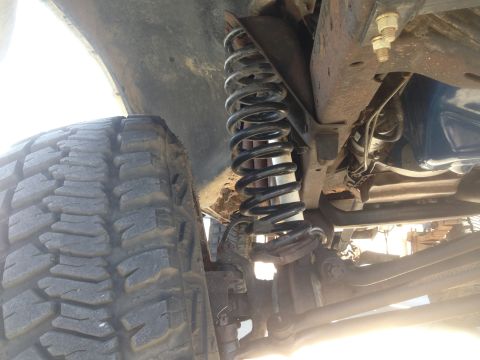 1979 Ford Bronco - This is a close-up, low-angle view of the undercarriage of a vehicle, focusing on the front suspension components. A large, aggressive trea…
