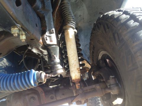 1979 Ford Bronco - A close-up, low-angle view of the undercarriage of a vehicle, focusing on the suspension components including a shock absorber, coil spring…