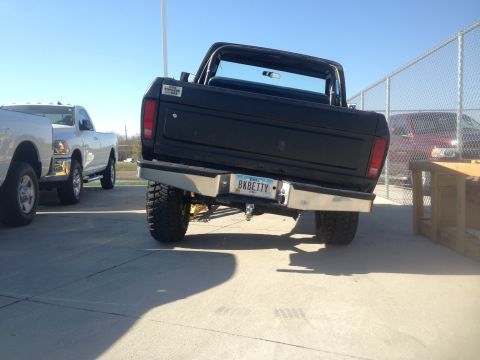 1979 Ford Bronco - The rear of a lifted black 1979 Ford Bronco is shown parked on a concrete surface. The vehicle has a custom license plate that reads "BKBET…