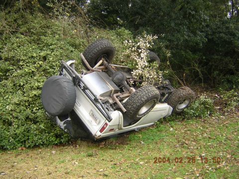 1984 Chevrolet Blazer - A white SUV has rolled onto its side in a grassy area surrounded by foliage.