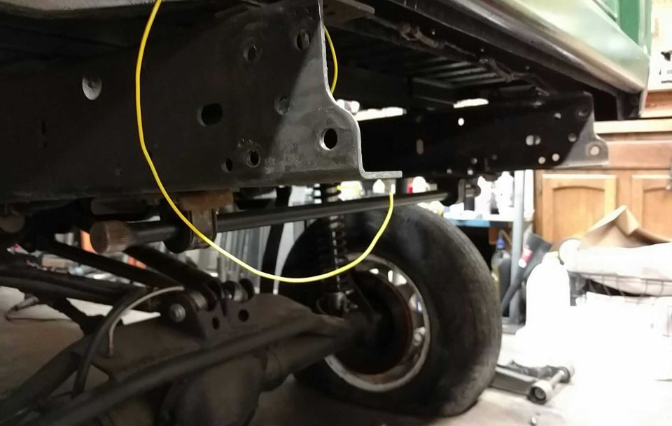 Underside of a vehicle frame with a yellow wire, tire, and suspension components.