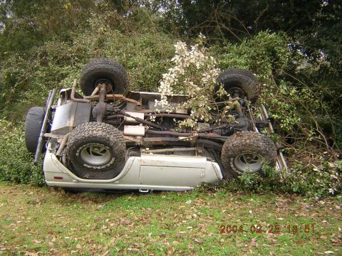 1984 Chevrolet Blazer - An overturned white SUV lies on its roof amidst dense vegetation, showing its undercarriage and tires.