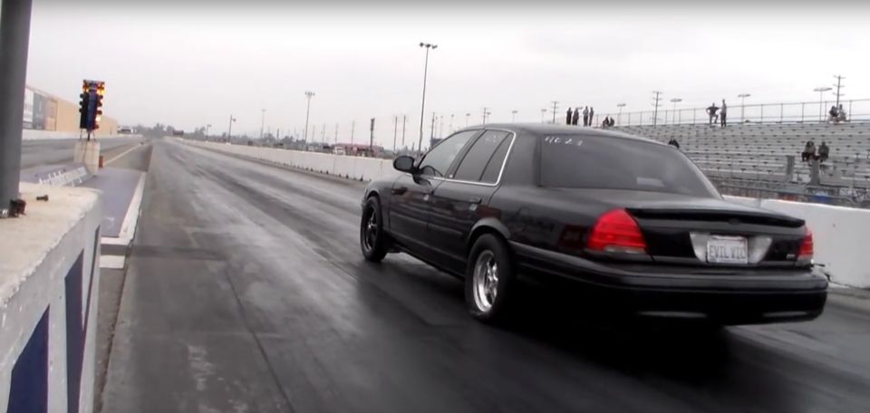 Black sedan launching down a drag strip