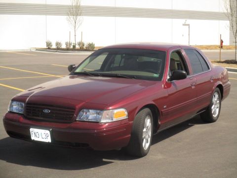 2004 Ford Crown Victoria - A maroon Ford Crown Victoria sedan is parked in an asphalt lot with yellow painted lines. The front license plate reads "FN3 L3P".