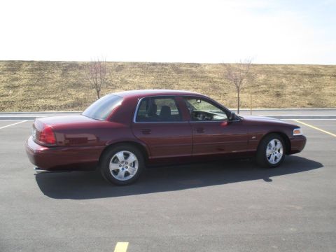 2004 Ford Crown Victoria - A maroon 2004 Ford Crown Victoria is parked on an asphalt lot with a grassy embankment in the background.