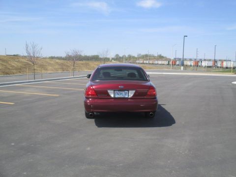 2004 Ford Crown Victoria - The rear view of a dark red Ford Crown Victoria is parked in an empty asphalt lot. The car's license plate reads "FN3 L3P".