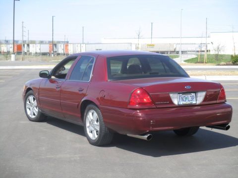 2004 Ford Crown Victoria - The rear passenger side of a maroon 2004 Ford Crown Victoria is shown parked in an asphalt lot. The car has a license plate that reads "FN3…
