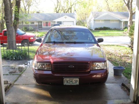 2004 Ford Crown Victoria - A maroon Ford Crown Victoria is parked in a driveway, facing the camera. A red Ford pickup truck is parked to the left of the Crown Victori…