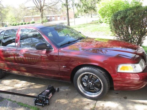 2004 Ford Crown Victoria - A dark red sedan is parked on a concrete driveway with a floor jack positioned underneath the front passenger side. The car has custom blac…