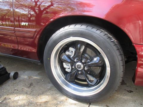 2004 Ford Crown Victoria - A close-up of the front passenger side wheel and fender of a dark red Ford Crown Victoria. The vehicle features a chrome and black aftermar…