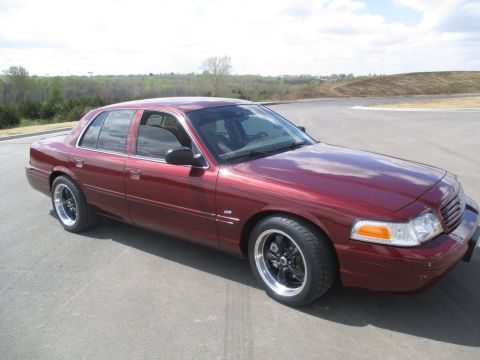 2004 Ford Crown Victoria - A dark red 2004 Ford Crown Victoria is parked on an asphalt surface with a slight curve. The car is shown from a 3/4 front angle, highlight…