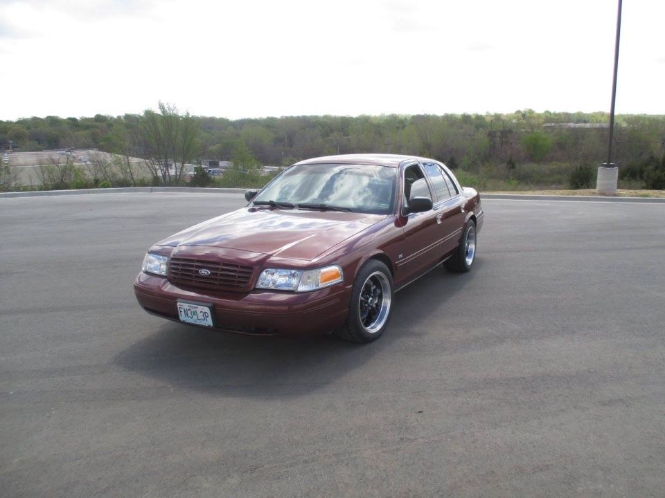 Maroon 2004 Ford Crown Victoria sedan with aftermarket wheels and license plate FN3-L3P parked on asphalt.