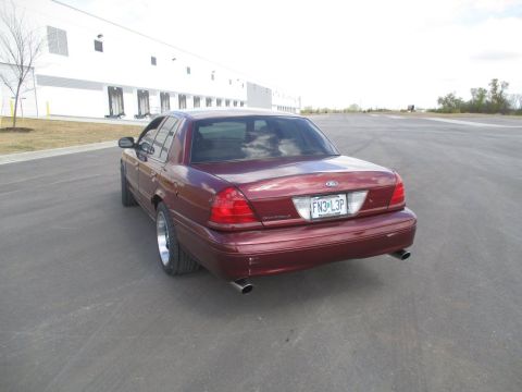 2004 Ford Crown Victoria - Rear 3/4 view of a maroon Ford Crown Victoria sedan parked on an asphalt lot with a large white building in the background. The car has chr…