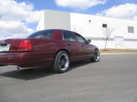 2004 Ford Crown Victoria - The rear passenger side of a maroon Ford Crown Victoria sedan is shown parked on asphalt in front of a modern industrial building with a bl…