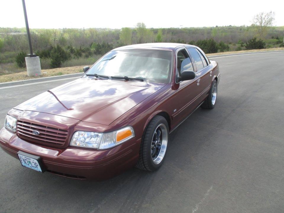 Maroon 2004 Ford Crown Victoria with custom wheels, parked on a road.