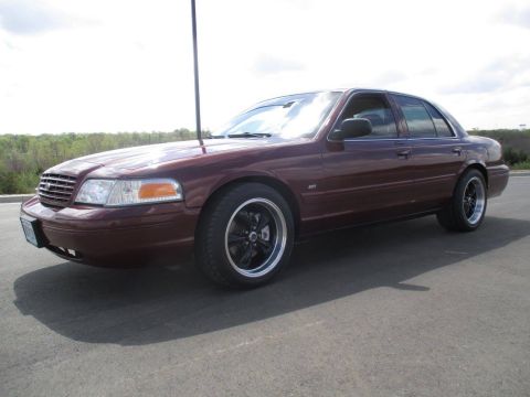 2004 Ford Crown Victoria - A maroon 2004 Ford Crown Victoria SVT is shown from a 3/4 front angle parked on an asphalt surface with a grassy tree line in the backgroun…
