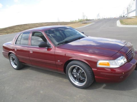 2004 Ford Crown Victoria - A maroon Ford Crown Victoria sedan is parked on an asphalt road with a slight incline. The car is shown from a 3/4 front angle, highlightin…