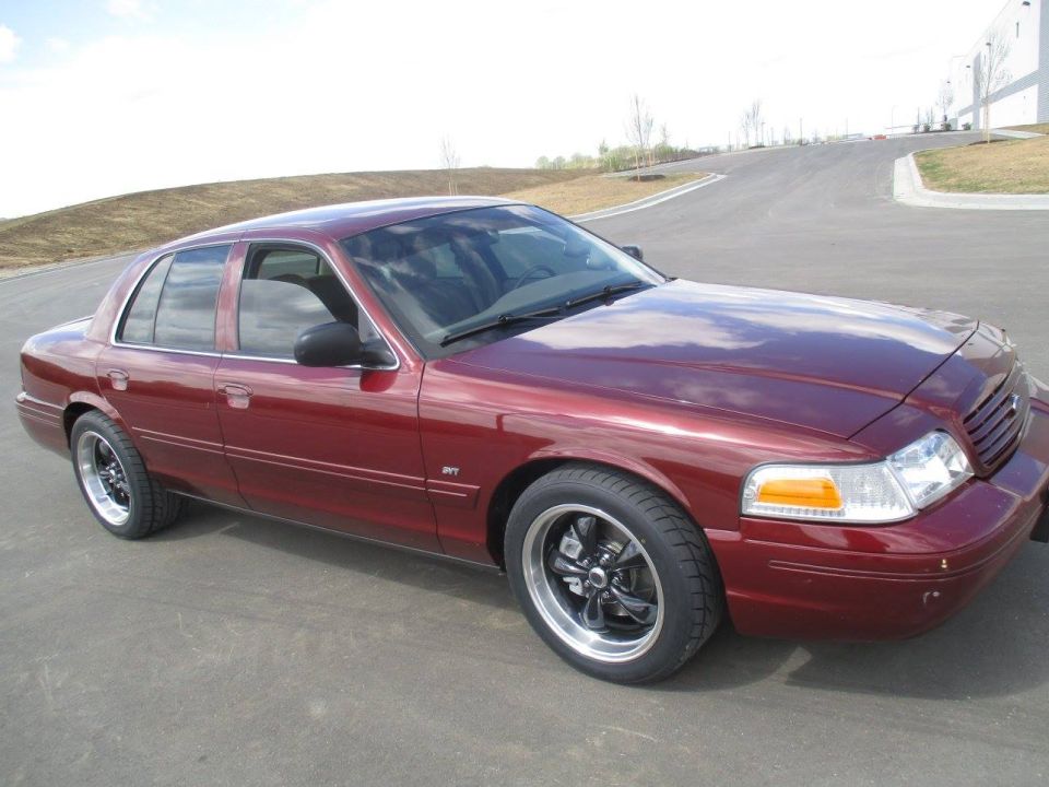 Maroon 2004 Ford Crown Victoria sedan with custom rims, parked on a road.