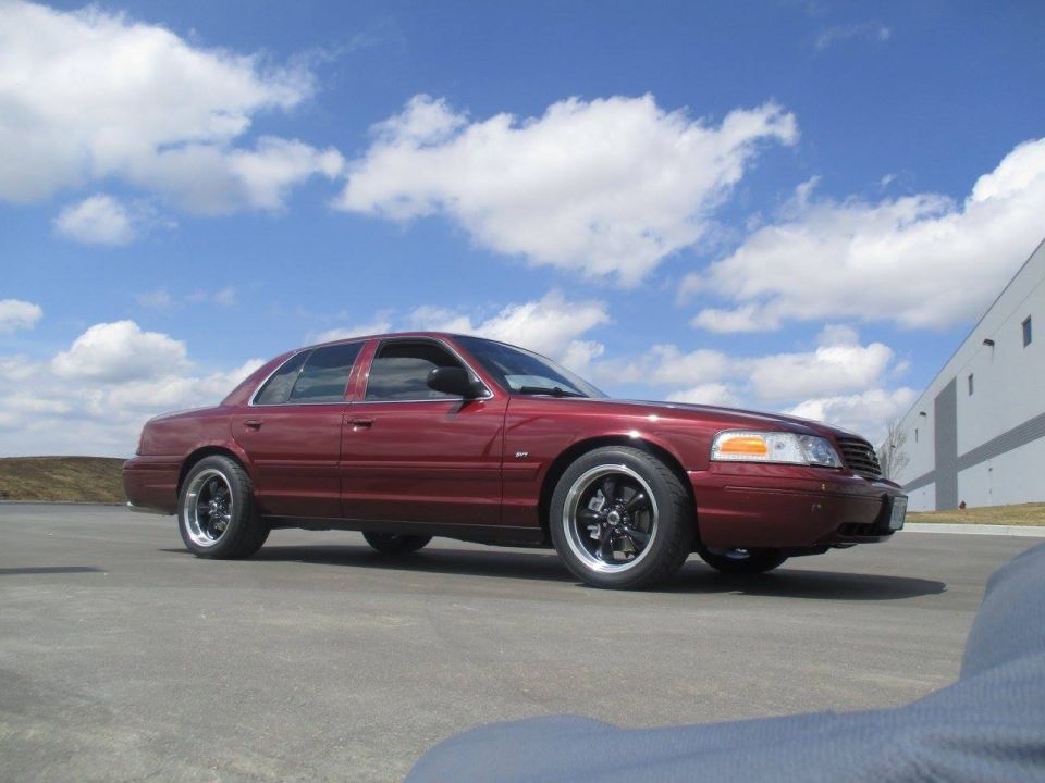 Maroon 2004 Ford Crown Victoria with custom black wheels, side view.