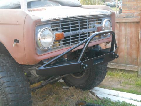 1972 Ford Bronco - A close-up, low-angle shot of the front of a vintage Ford Bronco, featuring a custom black aftermarket bumper with tow hooks and a winch cu…