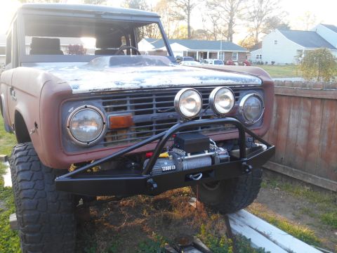 1972 Ford Bronco - A front 3/4 view of a classic Ford Bronco with a custom black bumper and winch. The vehicle has a weathered, rusty patina on the hood and f…