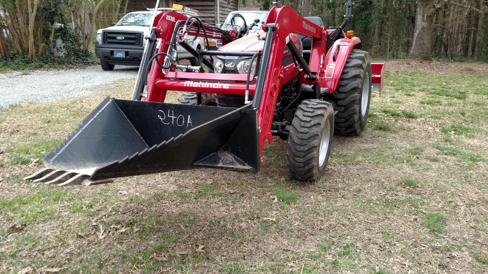 Red Mahindra tractor with front loader, white Ford pickup truck in background.