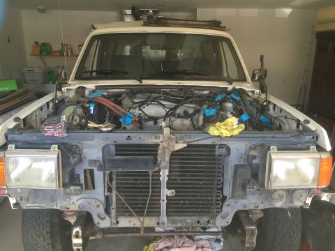 1987 Ford Bronco - Front view of a white Ford Bronco with its hood open, showing the engine bay disassembled in a garage. The grille and headlights are visibl…