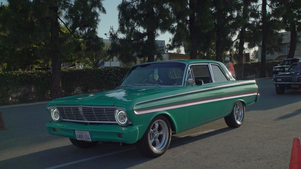 Green two-door sedan with chrome trim and aftermarket wheels, parked outdoors.